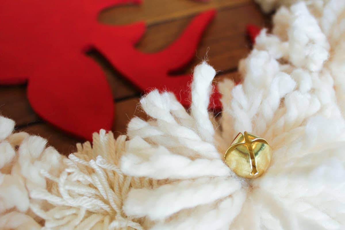 DIY Christmas wreaths are the best! The idea for this DIY Christmas wreath was inspired by a Pottery Barn wreath that costs $129! The DIY version takes less than an hour and is made using a wooden wreath form, DIY pom poms and some jingle bells. Click to view the full step-by-step tutorial. | MakeAndDoCrew.com