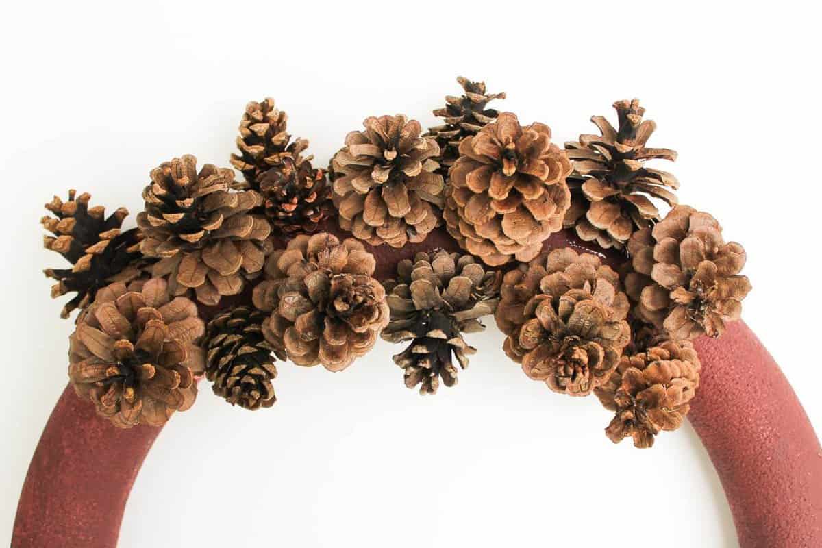 This DIY pinecone wreath is made with adorable little pom poms and costs less than $6 total! Perfect for the Christmas season and beyond. Click to view the full tutorial. | MakeAndDoCrew.com