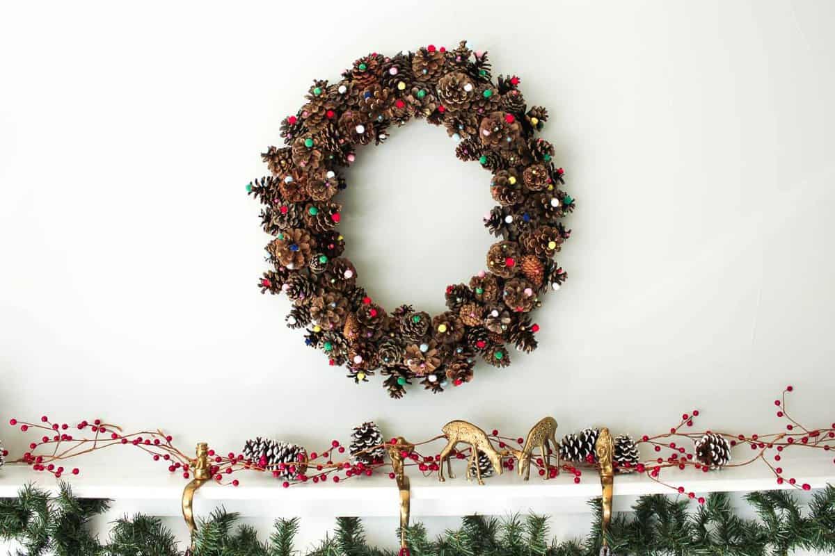 This DIY pinecone wreath is made with adorable little pom poms and costs less than $6 total! Perfect for the Christmas season and beyond. Click to view the full tutorial. | MakeAndDoCrew.com