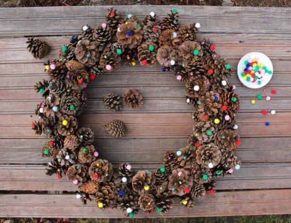 This DIY pinecone wreath is made with adorable little pom poms and costs less than $6 total! Perfect for the Christmas season and beyond. Click to view the full tutorial. | MakeAndDoCrew.com