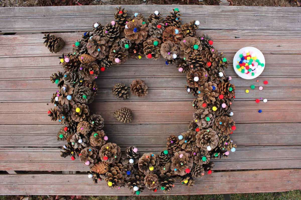 This DIY pinecone wreath is made with adorable little pom poms and costs less than $6 total! Perfect for the Christmas season and beyond. Click to view the full tutorial. | MakeAndDoCrew.com