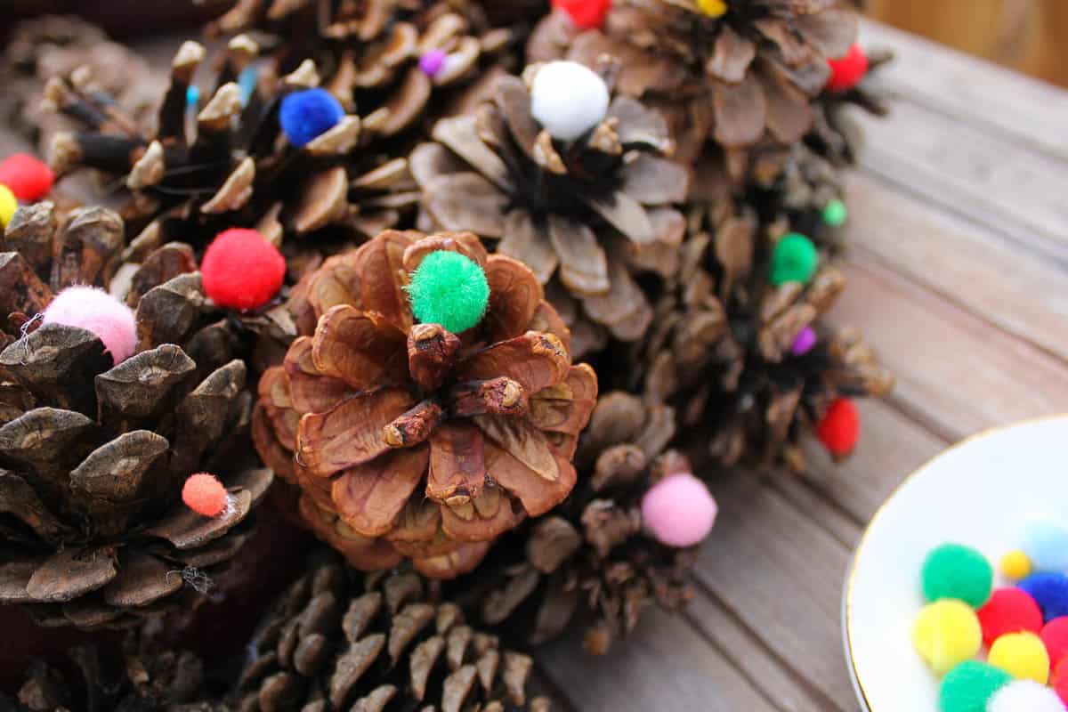 This DIY pinecone wreath is made with adorable little pom poms and costs less than $6 total! Perfect for the Christmas season and beyond. Click to view the full tutorial. | MakeAndDoCrew.com