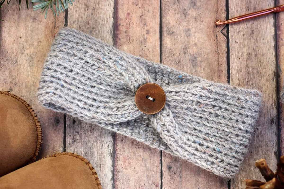 Crochet headband with a wooden button, laying on a rustic background.