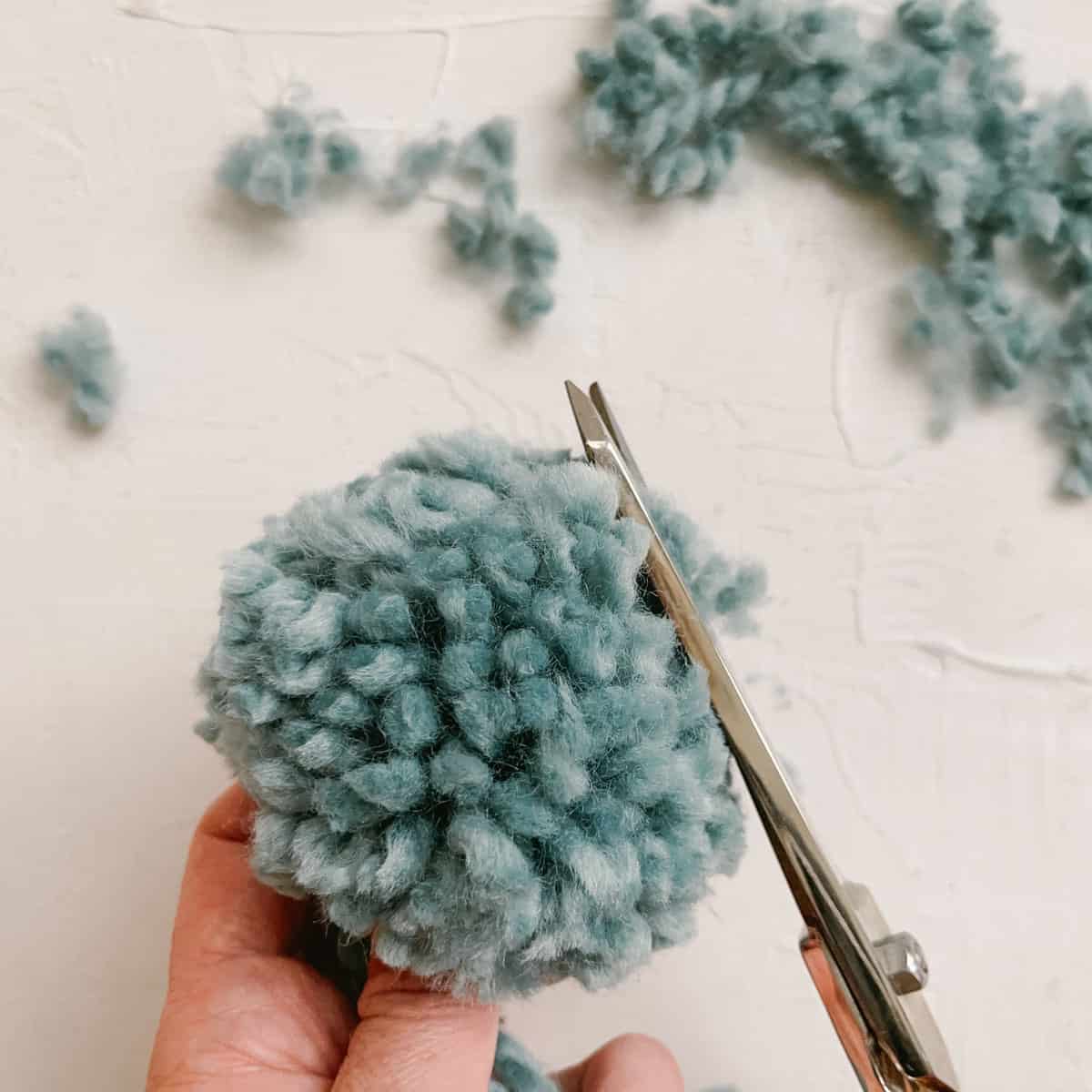 A handmade yarn pom pom being trimmed with gold scissors.
