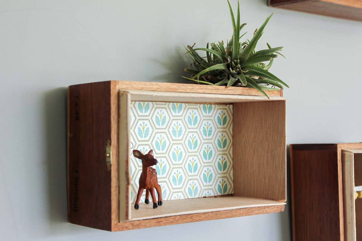 TUTORIAL: How to turn cigar boxes into floating DIY box shelves. This super easy home decor project can be done in about 15 minutes and looks great in a gallery wall. Perfect "art" idea for a nursery, playroom, bedroom or home office. | MakeAndDoCrew.com