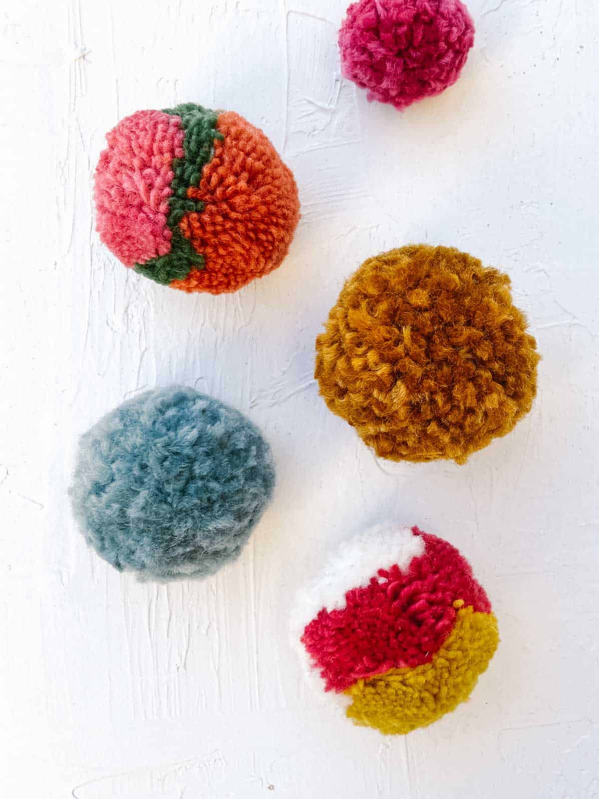 Multi-color pom poms in different sizes on a white plaster background.