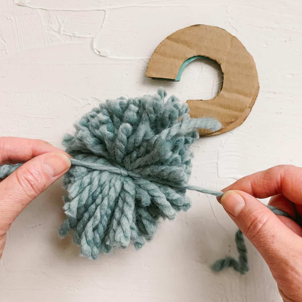 Tying off the strands of yarn in a handmade pom pom to secure them.