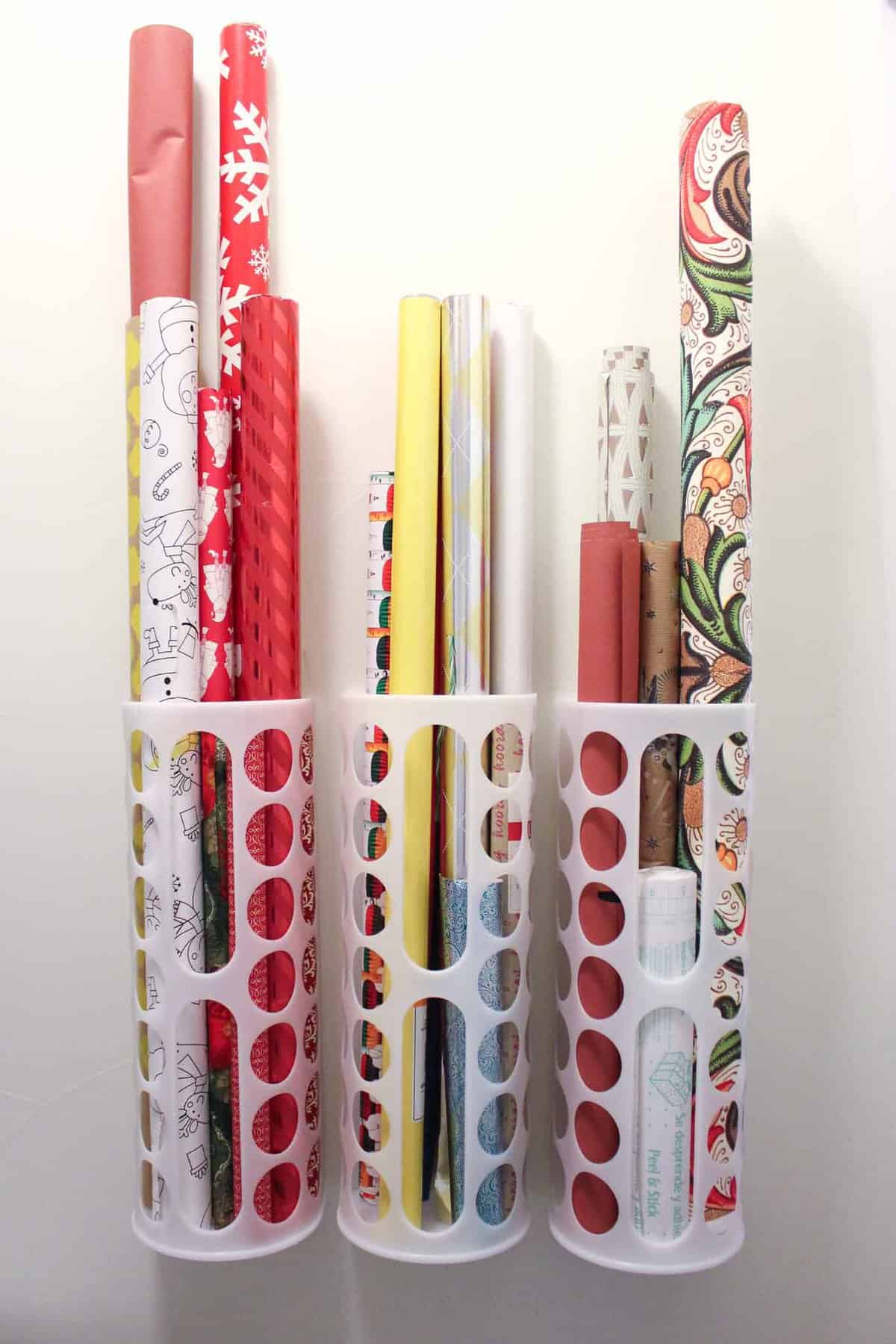 Rolls of wrapping paper stored vertically on a wall using IKEA's Variera plastic bag storage system.