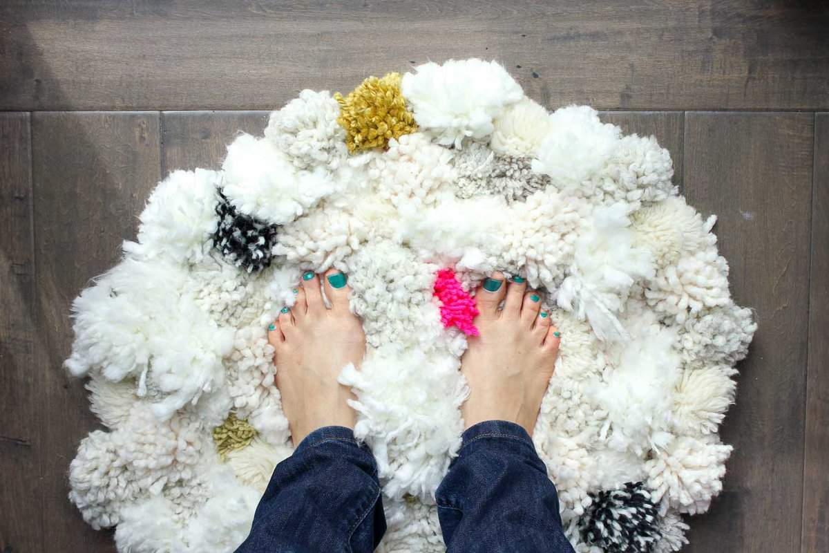 How to make a pom pom rug! This soft, scrumptiously squishy DIY pom pom rug takes very few skills to create and is a great way to use up a bunch of scrap yarn! Click for full tutorial. | MakeAndDoCrew.com