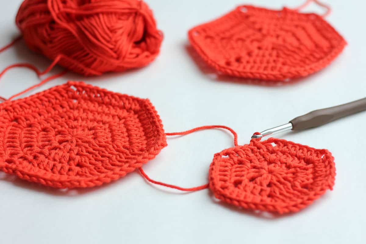 3 orange-colored basic crochet hexagon patterns in different sizes, a crochet hook, and a ball of orange yarn.