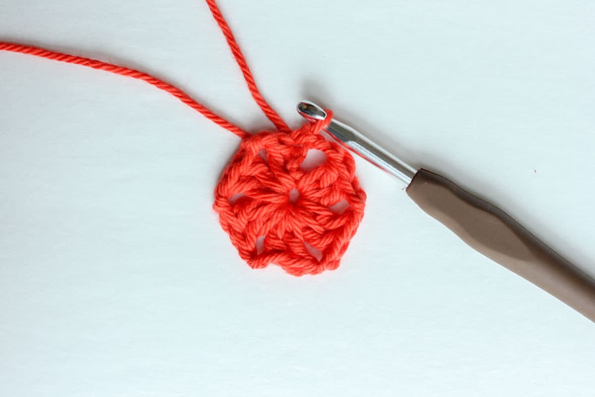 An orange yarn with a brown crochet hook showing the double crochet stitch.