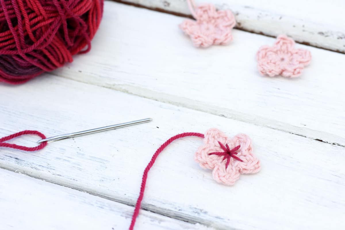 An almost done crochet cherry blossom pattern with a tapestry needle and yarn skein.