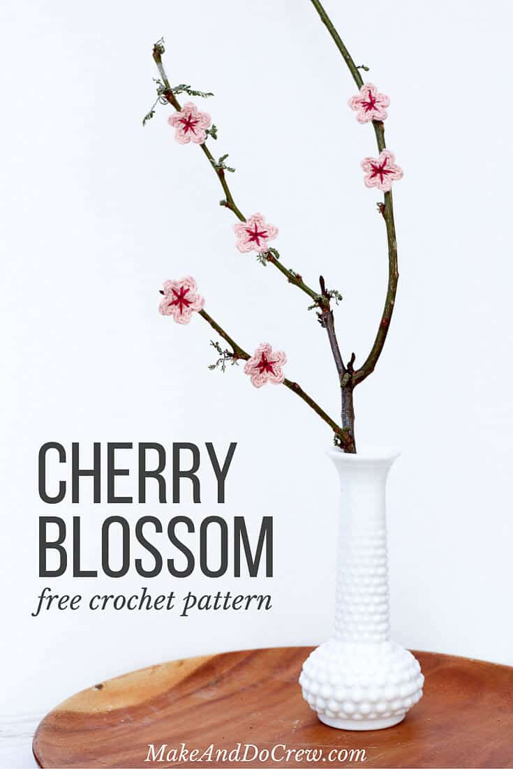 A crochet cherry blossom flower on a wooden branch inside a flower vase. 