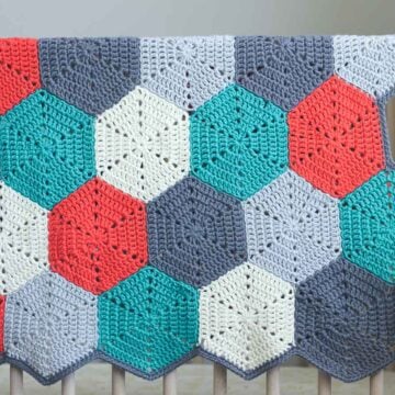 A crochet afghan made of hexagon shapes draped over a crib.