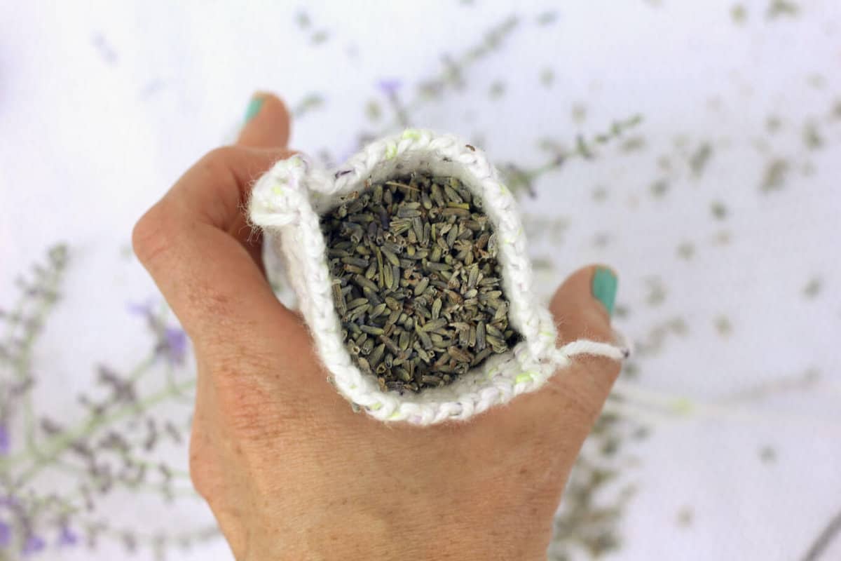 A hand holding an open crochet sachet pouch filled with lavender. 