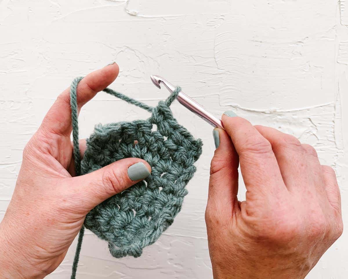 Demonstration of crochet knife grip using wooden crochet hook and green yarn.