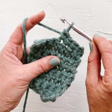 Hands demonstrating how to crochet a single crochet stitch.
