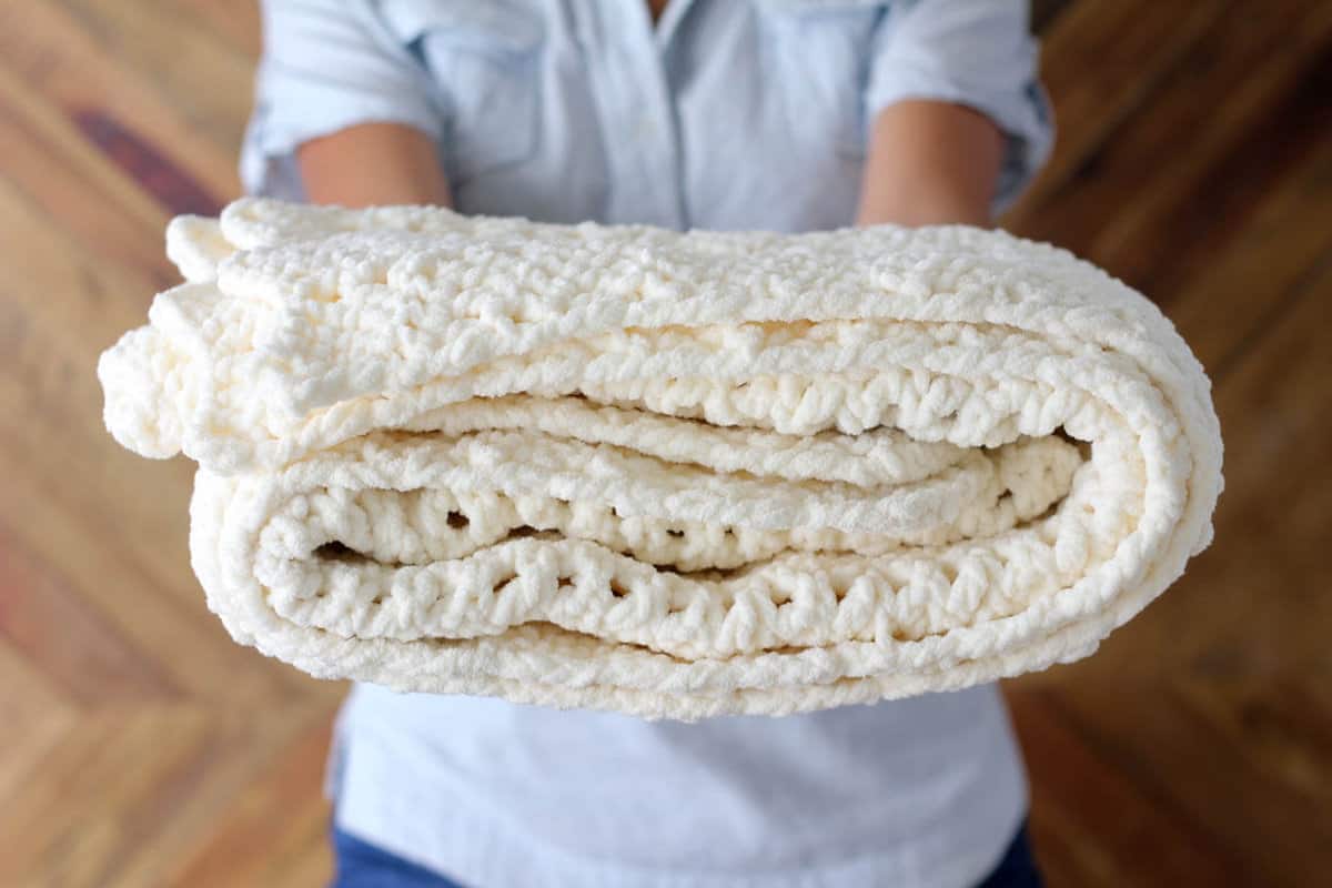 A woman holding a folded chunky crochet ripple blanket made with Bernat Blanket yarn.