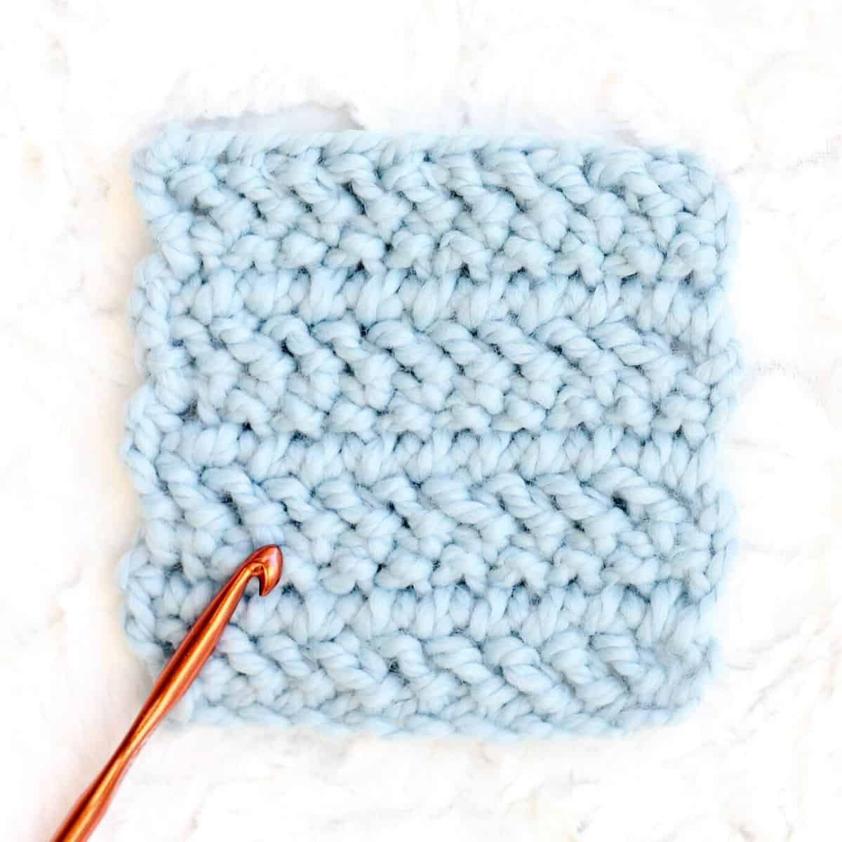 Beginner crochet blanket gauge swatch in chunky blue yarn.