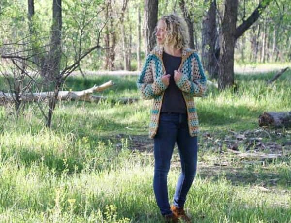 Believe it or not, two simple granny hexagons are the foundation of this free crochet hexagon sweater pattern. "The Campfire Cardigan" is made with Lion Brand New Basic 175 in Juniper, Cafe Au Lait, Thyme and Camel. Woman wearing modern crochet sweater in the forest.