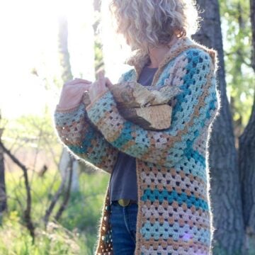 Blonde woman carrying firewood in the woods, wearing a crochet cardigan made from hexagons.