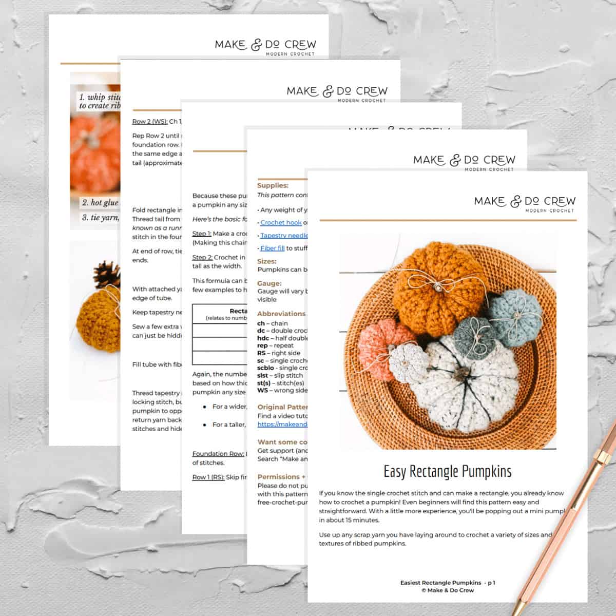 An overhead view of several pages of a printed crochet pumpkin pattern on a white rustic tabletop.