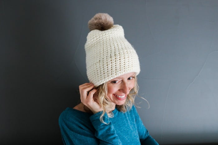Woman wearing a knit-look crochet beanie with a fur pom pom.