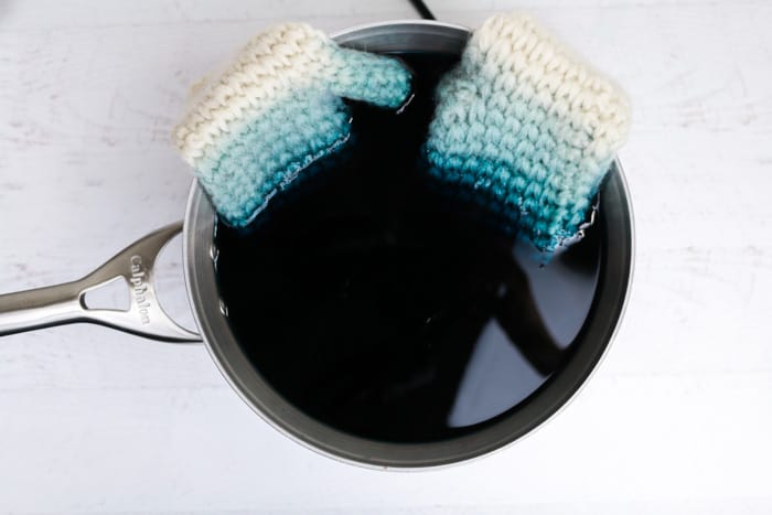 Learn an inexpensive trick to making any colored wool yarn you can imagine by using food coloring and vinegar for dye! Crochet mittens soaking in a dye bath.