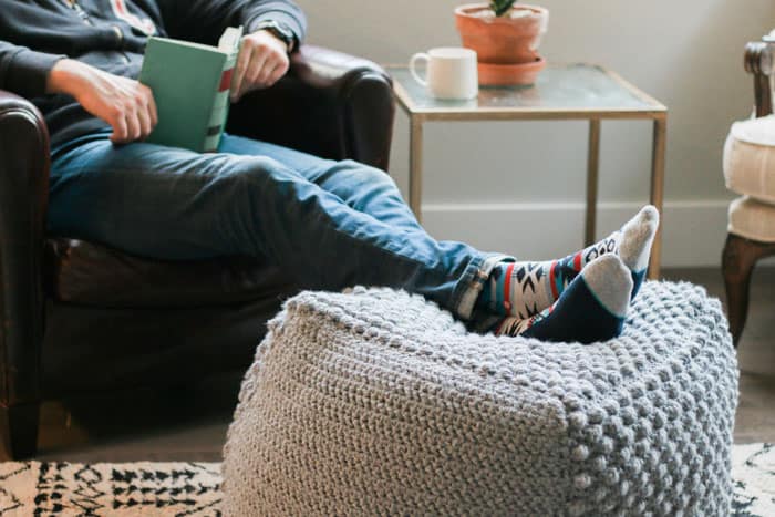 This free crochet pouf pattern makes an excellent foot stool or ottoman. Made with Lion Brand Pound of Love yarn in Oxford Grey. Free bean bag pattern from Make & Do Crew.