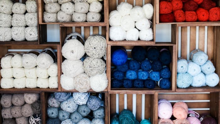 Lots of skeins of yarn organized by color on a bookshelf made from wooden crates.