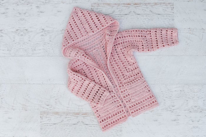 Child's crochet cardigan made from two hexagons. Free sweater pattern for girls features lace eyelets in pink Lion Brand Touch of Butta yarn.