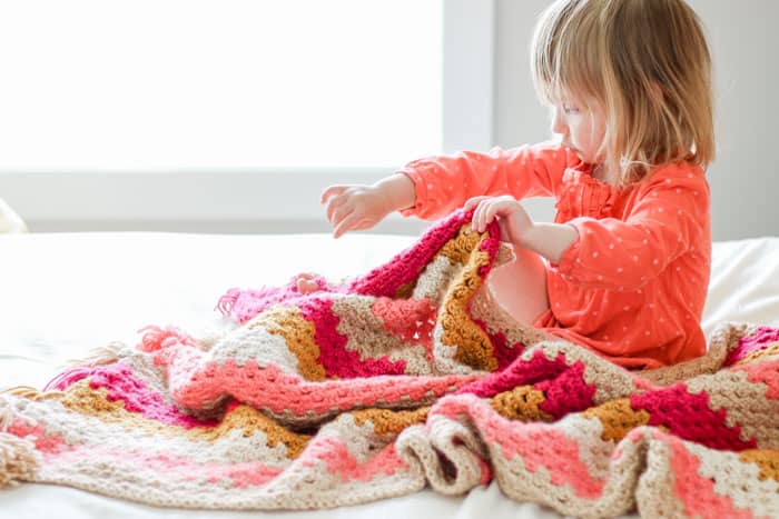 This modern crochet granny stitch baby blanket uses bold stripes and cheerful tassels to create a look that's perfect for kids' rooms and living rooms alike.