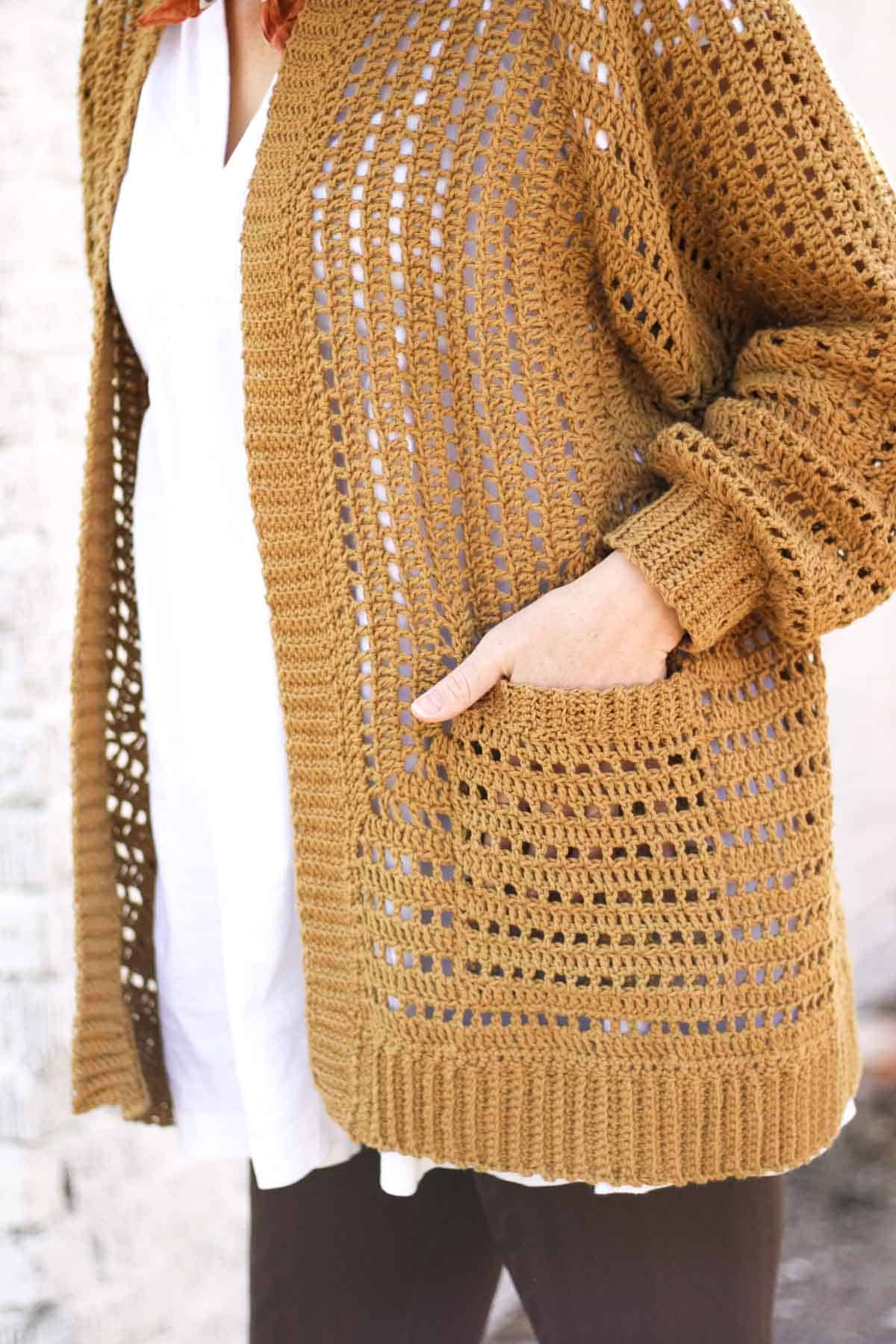 Hand placed in the pocket of a hexagon crochet cardigan.