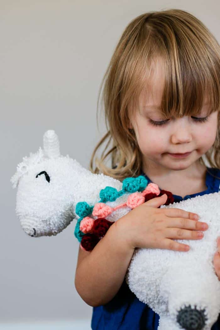 A young child holding a crochet alpaca toy made by hand. Free crochet amigurumi llama pattern.