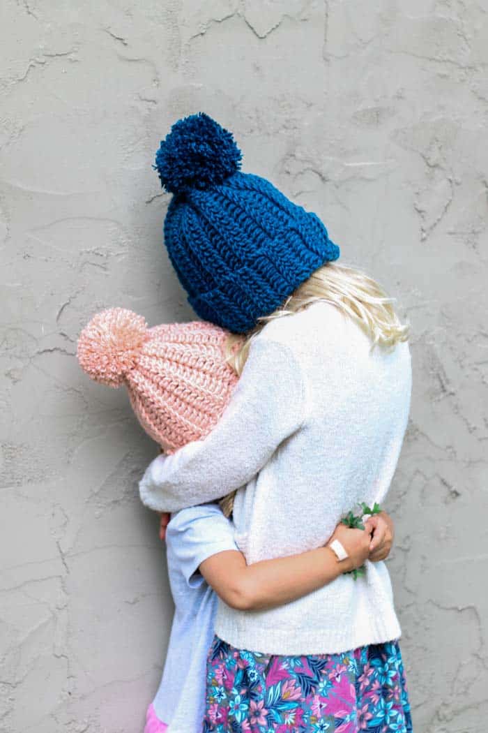 Two kids hugging while wearing a crochet toddler hat with pom poms.