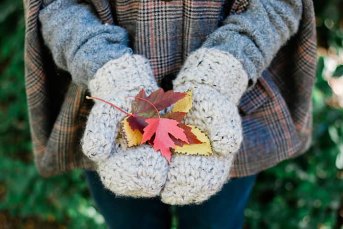 Chunky crochet wool mittens holding orange, yellow and red fall leaves. Free easy pattern and tutorial.