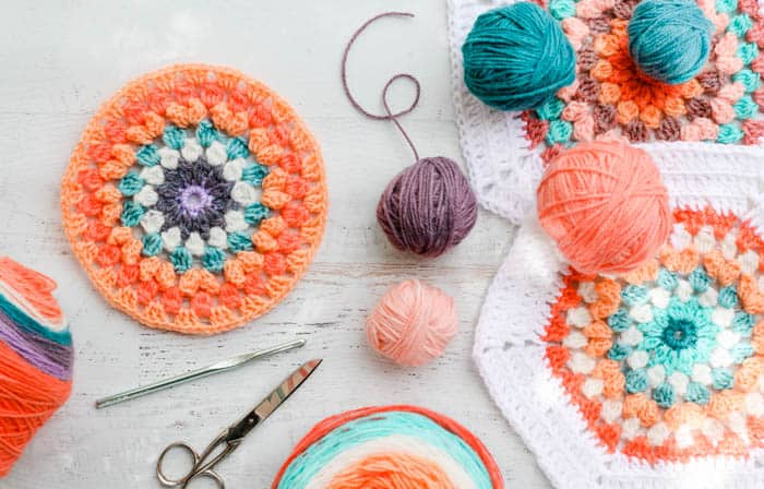 A few colorful balls of Mandala yarn laying on top of in progress crochet hexagons.