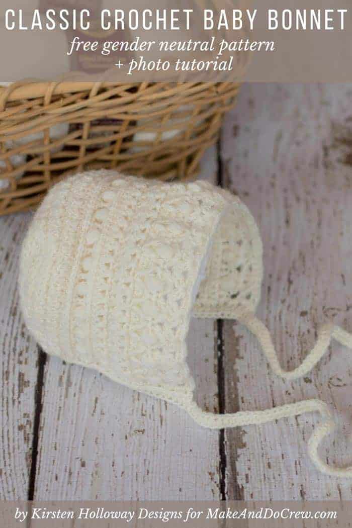 A gender neutral crochet baby bonnet with ties beside a wicker basket full of yarn skeins.
