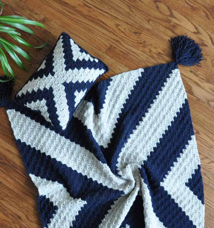 Navy blue and white crochet pillow and blanket displayed on hardwood floor. Free corner to corner crochet blanket and throw pillow pattern. 