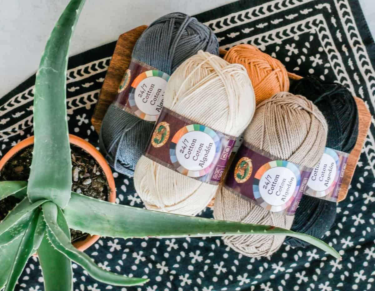 A pile of Lion Brand 24/7 Cotton yarn sitting next to a potted plant.