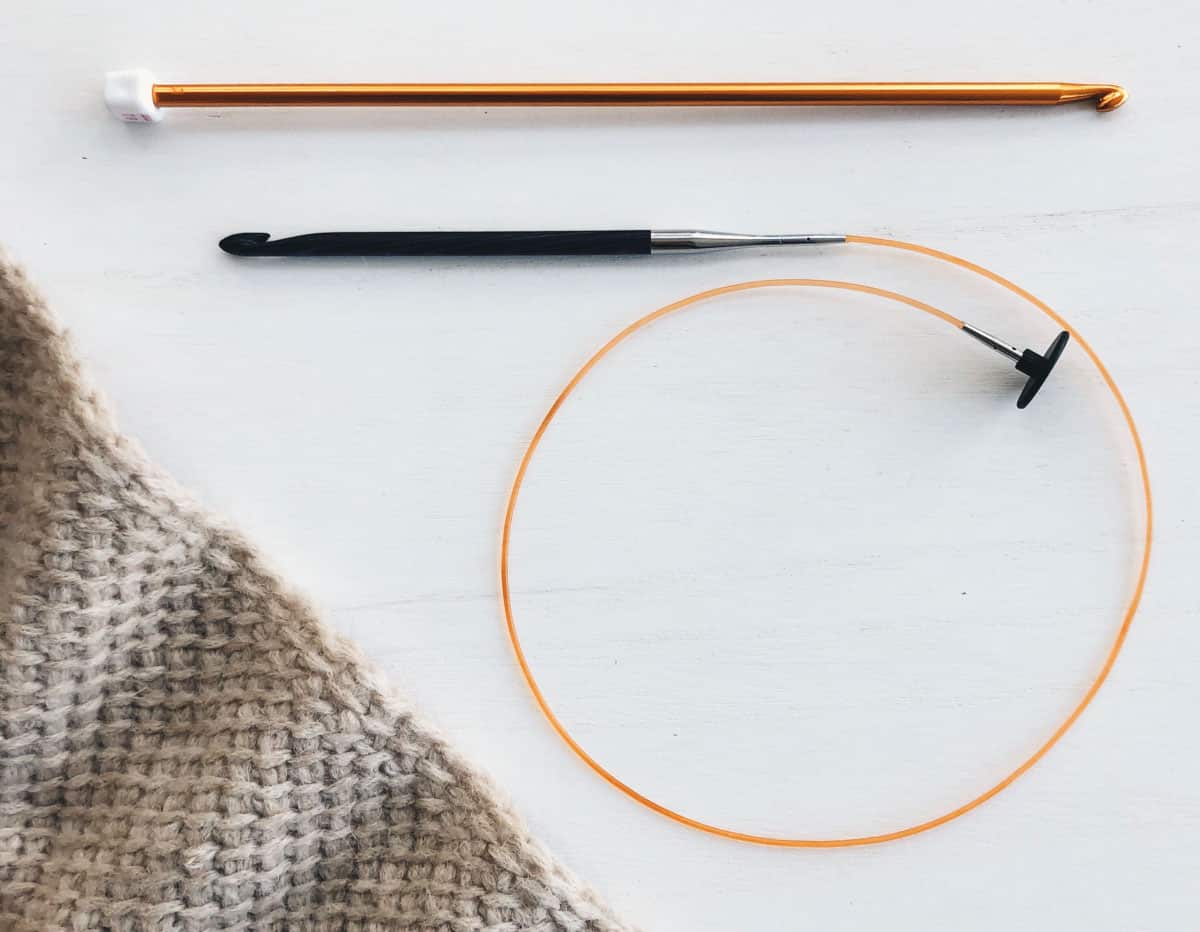 A long tunisian crochet hook (afghan crochet hook) alongside a tunisian crochet hook with a cable.