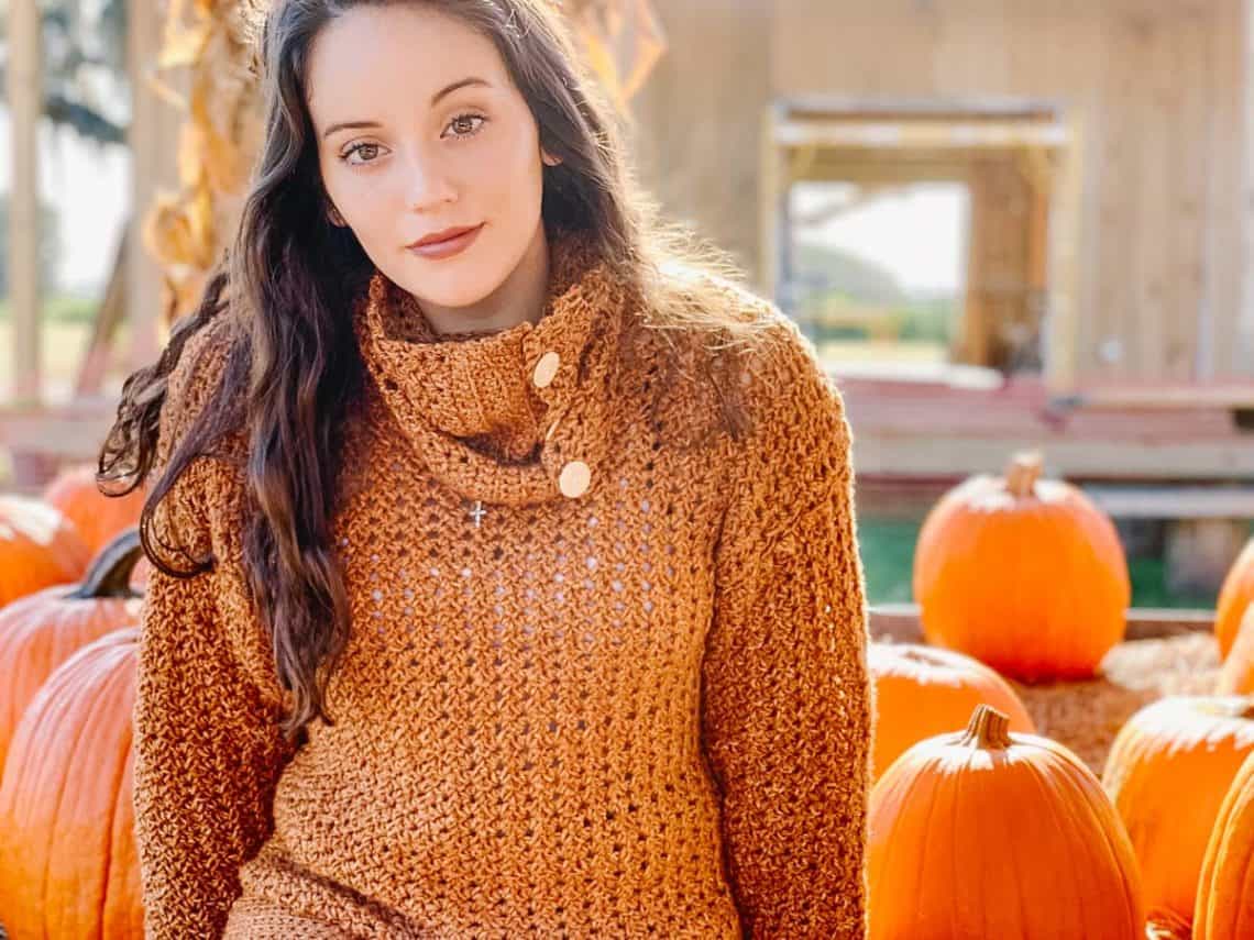 Girl sitting amongst pumpkins wearing an easy, crochet pullover sweater using Lion Brand Jeans yarn in the color Top Stitch.