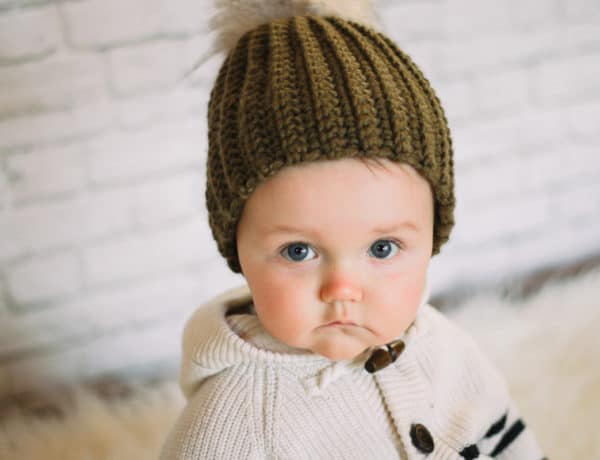 Adorable baby wearing a handmade crochet hat with a fur pom pom.