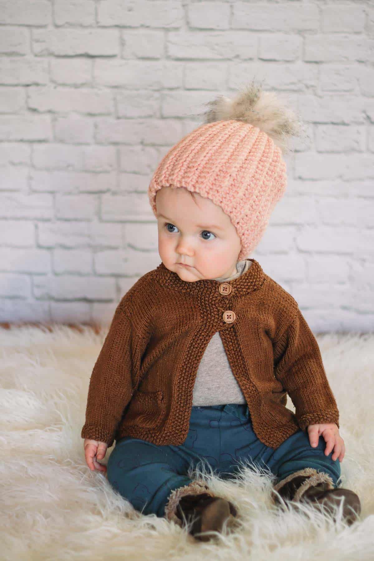 Young baby wearing a handmade crochet hat with a fur pom pom on top.