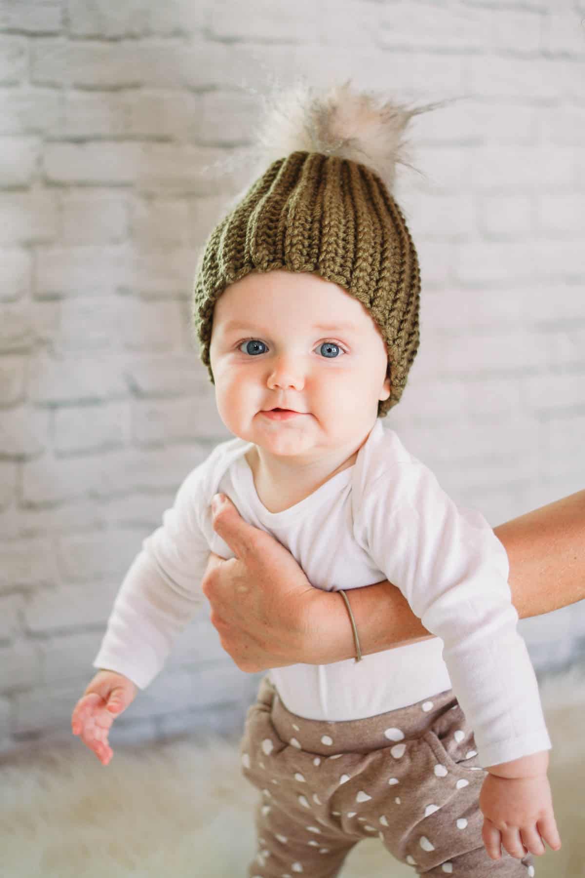 Baby wearing a modern, ribbed crochet beanie hat with fur pom pom on top.