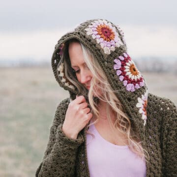 A blonde woman wearing a hooded crochet sweater featuring retro crochet granny square motifs in modern colors of Lion Brand Basic Stitch yarn.