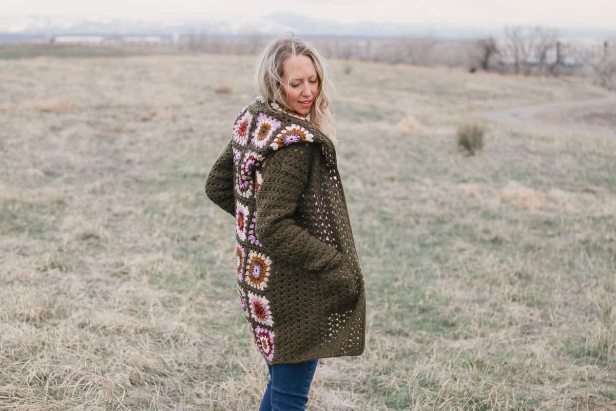 The back of a vintage-looking crochet granny stitch cardigan sweater with a hood.