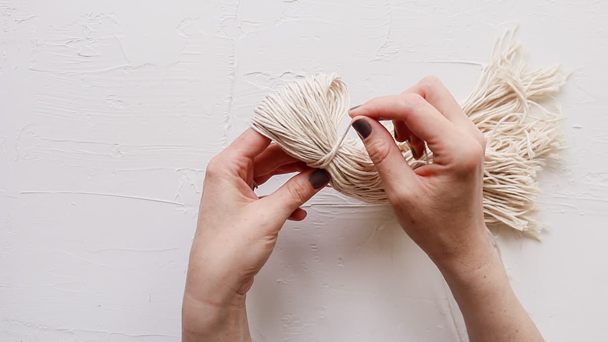 A close up of a woman's hands making a DIY yarn wall hanging with dollar store twine.