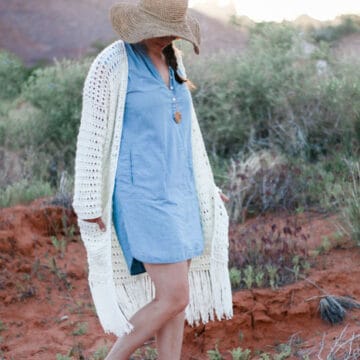 A woman standing in the desert wearing a long crochet cardigan with fringe.