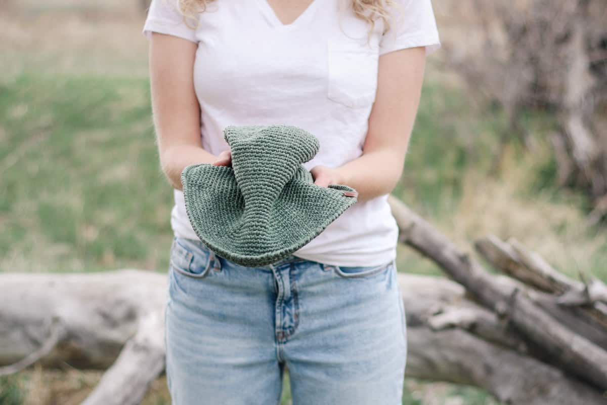 Woman squishing a crochet sun hat to show that it is very packable and floppy.